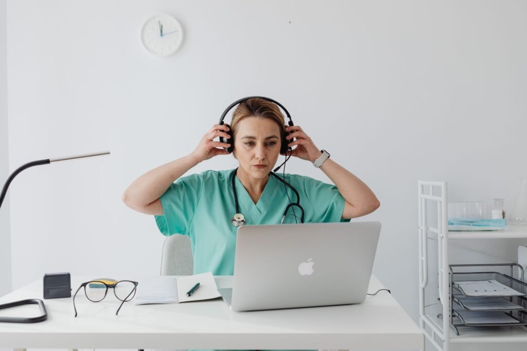 A doctor in scrubs with a headset, ready for an online consultation at a laptop