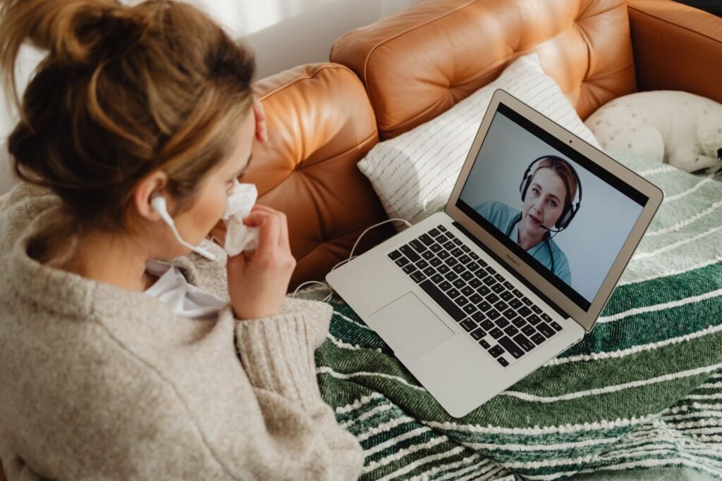 A patient at home on the sofa, talking to an online doctor on a laptop video call