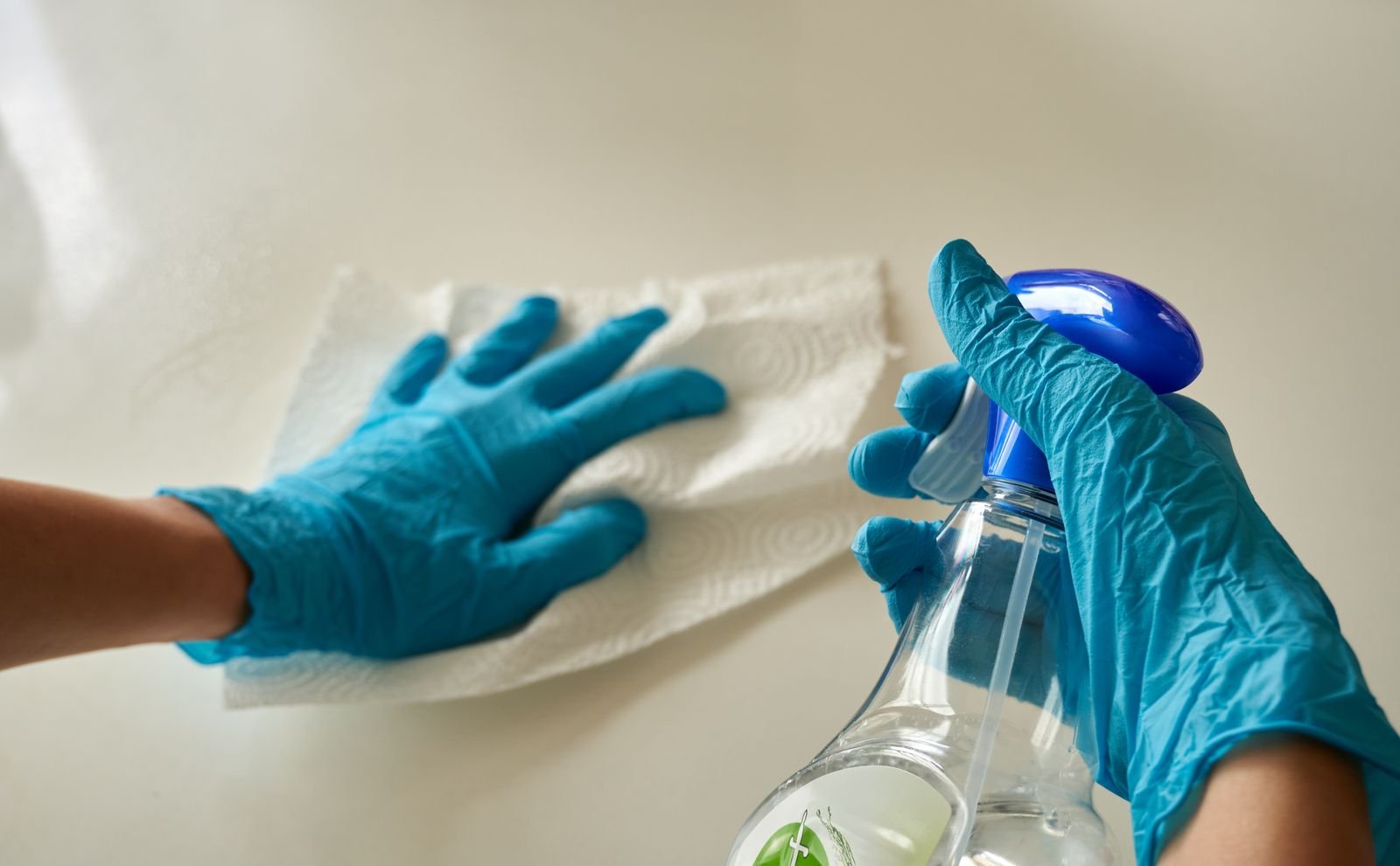 Gloved hands wiping a surface with a cloth and a spray bottle