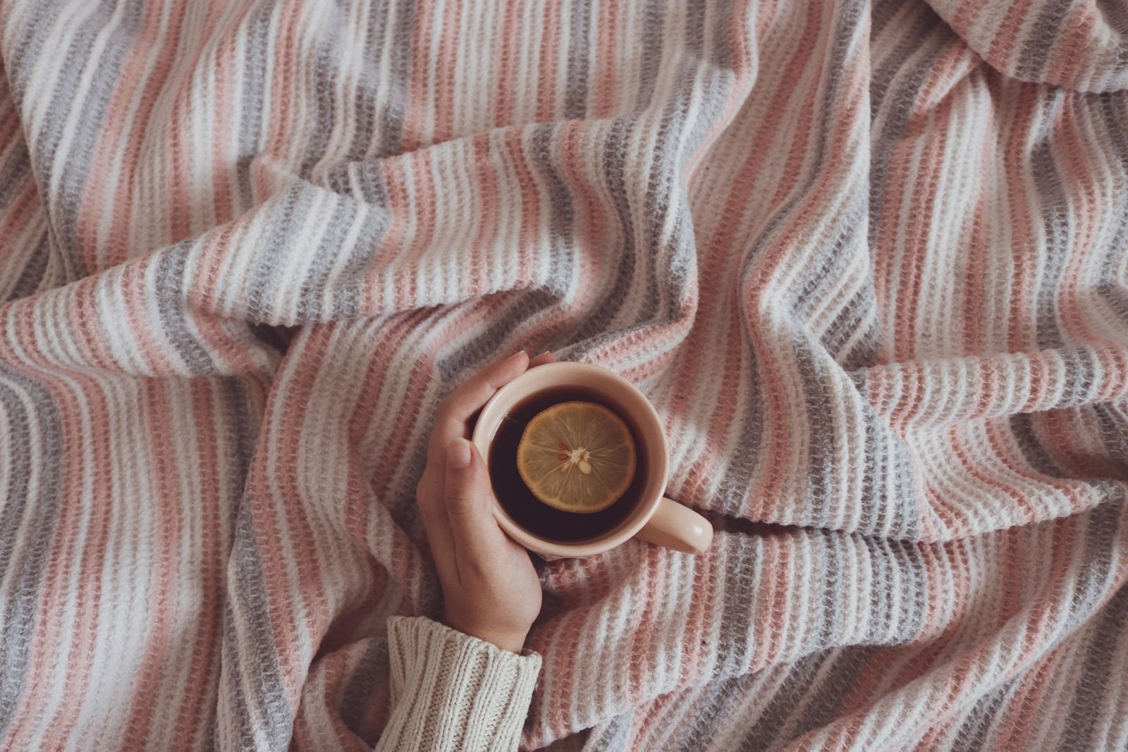 A hand holding a cup of tea with lemon on a striped blanket