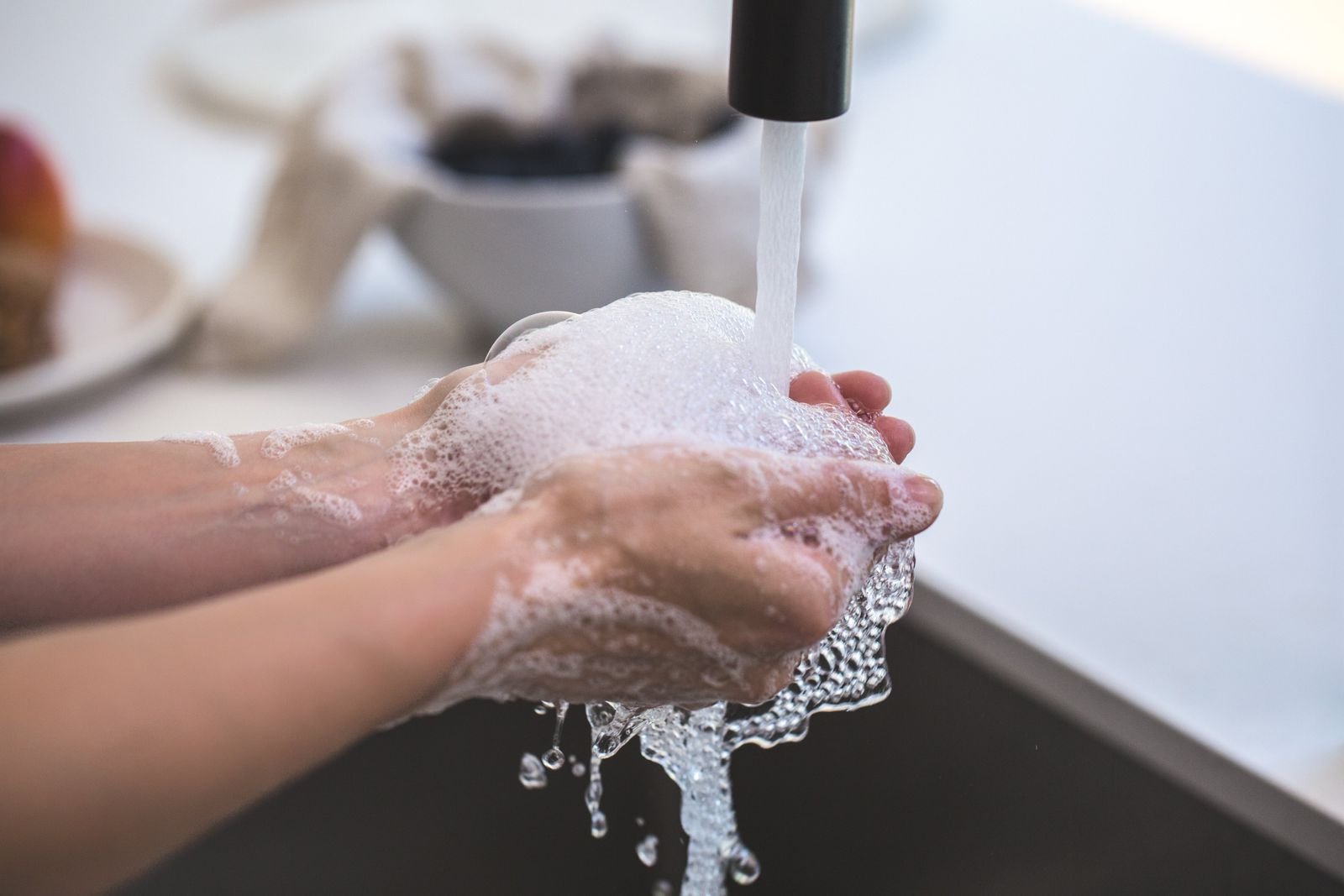 Hands being washed with soap lather under a running tap